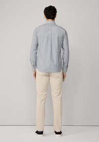 Camisa de rayas de manga larga en azul y blanco, con un cuello clásico y puños abotonados. Combinada con pantalones beige y zapatos oscuros.