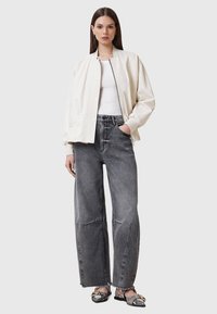 Cremefarvet bomberjakke med ribbede manchetter, båret over en hvid top, parret med høj talje og løse grå jeans og mønstrede sko.