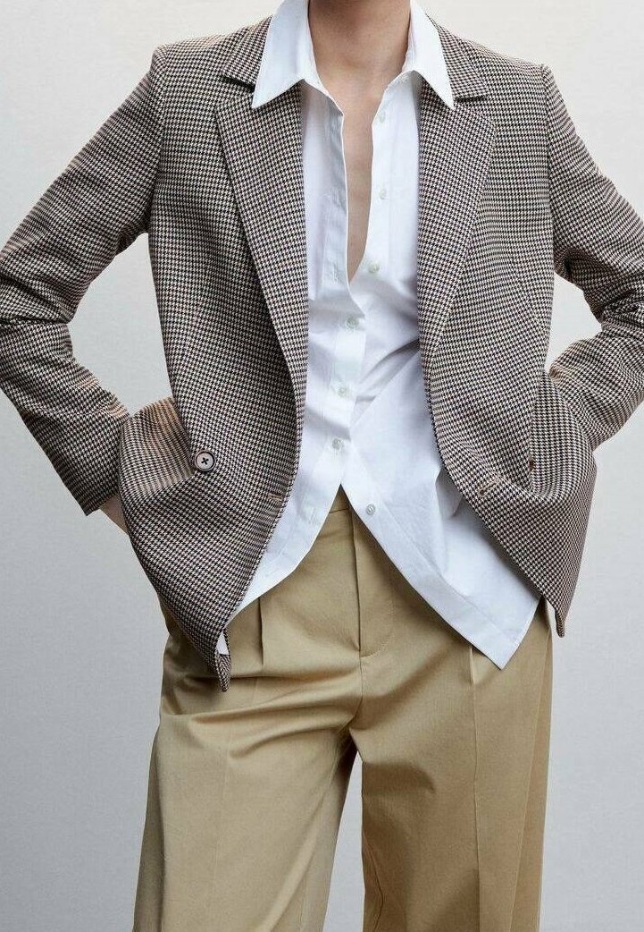 Blazer de cuadros marrones y beige con hombros estructurados, dos botones, combinado con una camisa blanca abotonada y pantalones beige.
