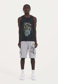 Black tank top featuring a colorful graphic design; gray cargo shorts with side pockets and dragon illustration. White sneakers complete the outfit.