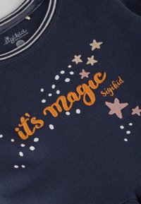 Marineblauer Sweatshirt mit weißem und orangem besticktem Text "Es ist Magie", umgeben von kleinen Sternen und Punkten in hellen Farben. Weicher Stoff.