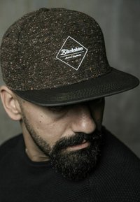 Brown patterned cap with a textured fabric, featuring a white diamond logo patch on the front and a black visor.