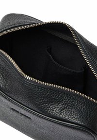 Svart läderpåse med en texturerad yta, med en guldfärgad dragkedja och en slät innerfoder. Innehåller inre fack för organisering.