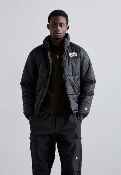 Svart pufferjakke med høy krage, med brodert "Billionaire Boys Club"-logo, kombinert med sorte cargo-bukser og en mørk skjorte.