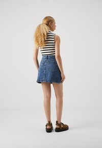 Denim mini seelik, millel on sobiv vöökoht ja kaks tagakotti; kombineeritud musta ja valge triibulise ilmavarrukatega pluusiga ja pruunide sandaalidega.