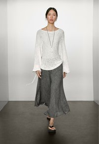 Maglione bianco a maniche lunghe con scollo ampio; gonna grigia fluida; sandali neri con plateau; indossato con una lunga collana; design minimalista.