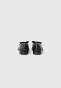 Black leather shoes with a smooth texture, rounded toe, and small bow accent at the heel. Flat rubber sole and minimal design.