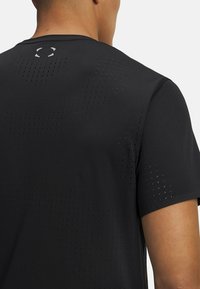 Sort atletisk t-shirt med en åndbar struktur og små perforeringer, rund halsudskæring og et reflekterende logo på ryggen.