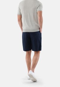 Jasnoszary krótki sweter z dzianiny z krótkim rękawem w zestawieniu z granatowymi szortami. Białe sneakersy dopełniają swobodny wygląd, podkreślając komfort i prostotę.