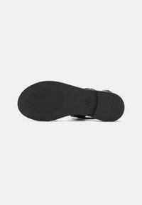 Suela de zapato plano negro con una superficie lisa, patrón de agarre texturizado y soporte de arco moldeado. Presenta correas ajustables para un mejor ajuste.