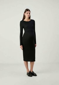 Vestido preto, de manga longa, justo ao corpo, com comprimento midi, desenhado para acomodar uma barriga de gravidez, textura suave, gola redonda simples.