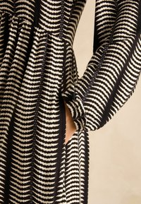 Vestido con un estampado de rayas blancas y negras, hecho de una tela texturizada con una cintura fruncida y bolsillos laterales. Incluye mangas largas.