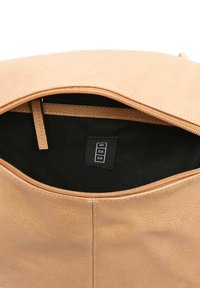 Smėlio spalvos odinė petneša su tekstūruotu paviršiumi, juodo audinio vidus ir užtrauktuko užsegimas. Raktelis su matoma prekės ženklo pavadinimu.