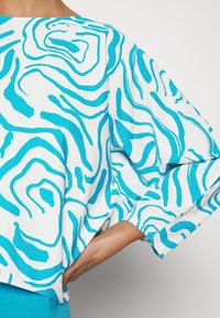 Camicia a maniche corte blu e bianca con un motivo astratto ondulato; tessuto leggero con una vestibilità rilassata e maniche ampie.