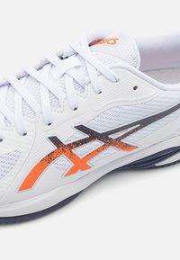 Zapatilla deportiva blanca que cuenta con una parte superior texturizada y transpirable, acentos en naranja y negro, y una suela acolchada con un diseño elegante.