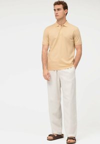 Polohemd in hellem Beige, kurze Ärmel, Knopfleiste mit drei Knöpfen. Kombiniert mit weißen Leinenhosen und braunen Sandalen. Lässige Passform.