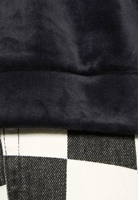 Gros plan sur des textures de tissu montrant un matériau noir lisse au-dessus d'un tissu tissé à carreaux noir et blanc avec des coutures visibles.