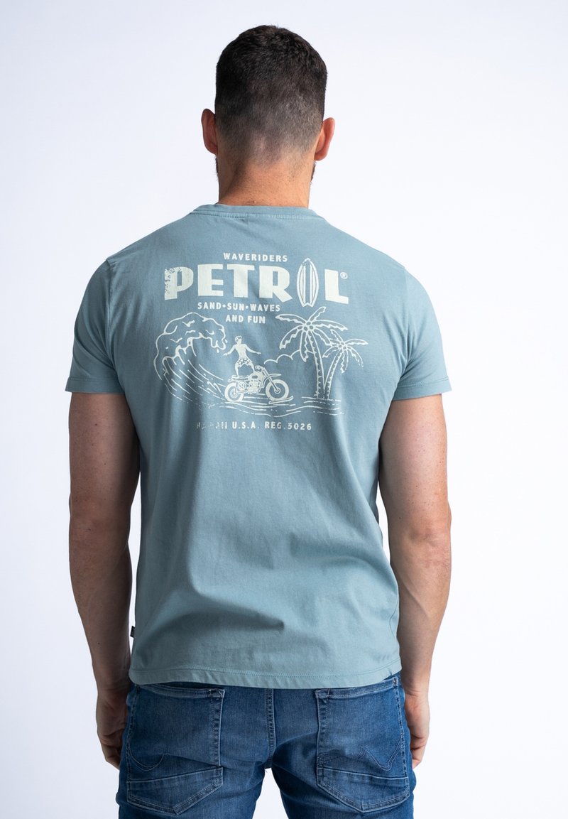 Lichtblauwe t-shirt met korte mouwen en een grafische print van surf, palmbomen en de tekst "PETROL WAVERIDERS." Zachte katoentextuur.