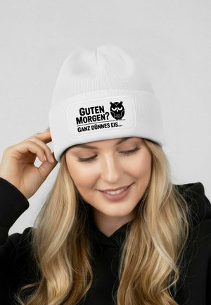 White knitted beanie with a rectangular black patch featuring the text "GUTEN MORGEN? GANZ DÜNNES EIS..." and an owl graphic.