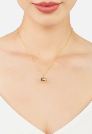 Gold necklace with a round pendant featuring a textured surface and a purple accent. Chain is twisted design, resting on bare skin.