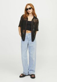 Zwarte netten knoopblouse over een zwarte cropped top, gecombineerd met lichtblauwe wijde jeans en zwarte sandalen.