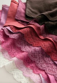 Pile de sous-vêtements en tissu doux dans des tons marron, rouge, rose et lavande, avec une bordure en dentelle festonnée le long des bords.