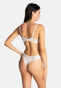 Ensemble de lingerie en dentelle blanche avec un motif floral, des bretelles ajustables et une coupe taille basse avec des bords festonnés sur la ceinture.