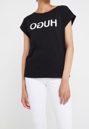 Czarna koszulka z bawełny, z krótkimi rękawami i białym nadrukiem logo "HUGO" ustawionym do góry nogami. W połączeniu z białymi jeansami.