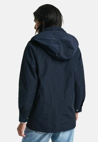 Marinblå tygjacka med huva, med elastiska ärmslut och dragsko i midjan. Slät textur med en minimalistisk design.