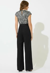 Czarne spodnie typu wide-leg w połączeniu z metaliczną srebrną bluzką z cekinami, z krótkimi rękawami i detalem w kształcie keyhole na plecach. Całość o gładkiej fakturze.