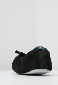 Black felt slipper with a rounded shape, soft texture, and a small heel tab featuring a blue and yellow accent.