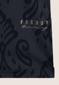 Tessuto blu scuro con un motivo damascato testurizzato. Presenta il nome del marchio "FREDDY" in grassetto oro metallico e una scritta in corsivo "training" sottostante.