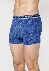Blaue Boxershorts mit einem geometrischen Muster aus dunkelblauen Linien. Mit einem schwarzen Bund, auf dem "KOROSHI" in Weiß gedruckt ist. Dehnbare Stoffqualität, eng anliegende Passform.
