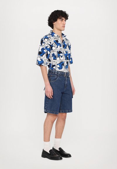 Cămașă cu mânecă scurtă în alb și albastru cu un model geometric; asortată cu șorturi din denim până la genunchi și pantofi slip-on negri.