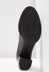 Botte en cuir noir avec un petit talon carré, semelle en caoutchouc texturé et détail de couture contrastant sur le côté. Fini supérieur lisse.