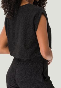Top nero a maniche corte con finitura tessutata e scintillante, dal taglio ampio, abbinato a pantaloni a vita alta coordinati.