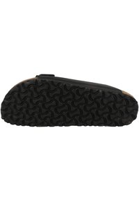 Chaussure noire avec une semelle en caoutchouc texturée présentant un motif ondulé. L'empeigne a une finition lisse et une forme légèrement arrondie.