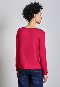 Langärmlige, fuchsiafarbene Bluse mit lockerer Passform, glattem Textur und weitem Ausschnitt. Kombiniert mit dunkelblauen Jeans, was einen lässigen Look zeigt.