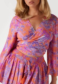Yläosa ja matching hame kirkkaan oranssissa ja violetissa paisley-kuosissa. Sisältää smockatuin vyötärölinjain ja oranssin tupsun yksityiskohtana.