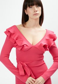 Abito aderente di un vivace colore rosa, con scollatura arricciata e maniche lunghe, dotato di una cintura in vita per la regolazione. Tessuto liscio ed elastico.