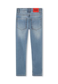 Jeans de mezclilla de color azul claro con un corte ajustado. Presenta dos bolsillos traseros y una etiqueta del logo HUGO de color rojo brillante en la cinturilla. Textura suave.