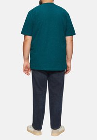 Tiefblaues T-Shirt mit kurzen Ärmeln und gesprenkeltem Muster, kombiniert mit dunkelblauen, geraden Hosen und beigen Schuhen, aus der Rückansicht.