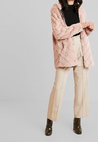 Abrigo de piel sintética rosa con un patrón texturizado, corte oversized y capucha. Combinado con pantalones de talle alto beige y botines negros brillantes.