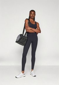 Svart atletisk drakt med tanktop-design og tettsittende ben, kombinert med en liten svart veske med mesh-detaljer, brukt med hvite joggesko.