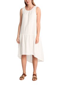 Weißes Leinenkleid mit U-Bootausschnitt und ärmellosem Design. Verfügt über einen mehrstufigen Saum mit einem hohen Front- und niedrigem Rückenteil. Kombiniert mit braunen Sandalen.