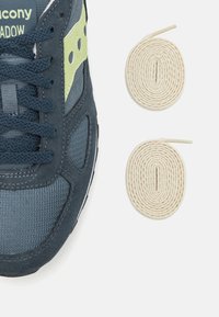 Sötétkék sneaker szürke hálós és velúr panelekből, zöld részletekkel és fekete talppal. Két krémszínű fűzőopció mellett található.