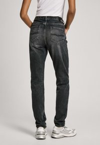 Svarta denimjeans med slim fit, med två bakfickor och en logotyp på midjebandet, i kombination med grå sneakers.