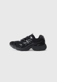 Schwarzer Sportschuh aus Mesh-Material mit synthetischen Akzenten, runder Zehenpartie, strukturiertem Profil und kontrastierenden glänzenden Details im Obermaterial.