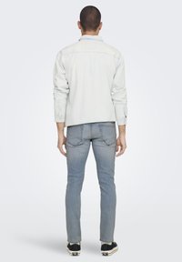 Chaqueta de mezclilla gris clara con mangas largas y puños abotonados, combinada con jeans ajustados de color azul claro y zapatillas negras con suelas blancas.