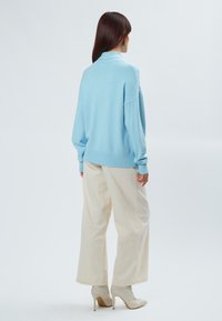 Maglione oversize azzurro chiaro con bordo costine, abbinato a pantaloni ampi crema e stivali con tacco alto beige, visto da dietro.